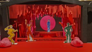 Design of Hairy set. Red fridge lines the stage while people in single coloured morph suits stand on the red floor. 