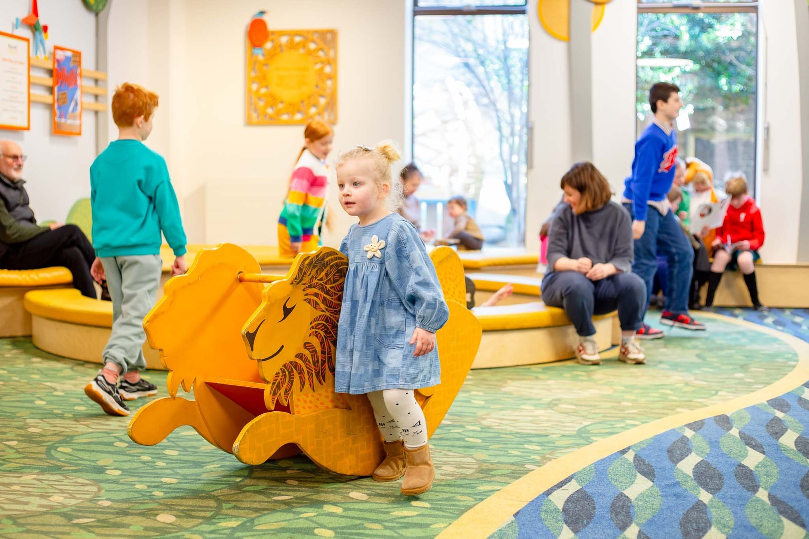 A child with a wooden rocking seat shaped like a lion.
