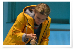 Layla Bradbeer (blonde hair tied back in a yellow coat) operates a puppet