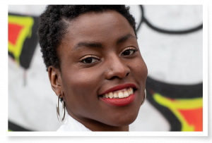A headshot of Farrell Cox (short dark hair, white t-shirt and silver hoop earrings)