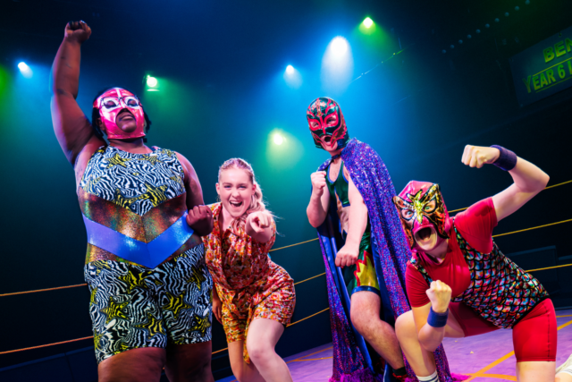 A group of wrestlers in a wrestling ring with their arms out, wearing wrestling masks.