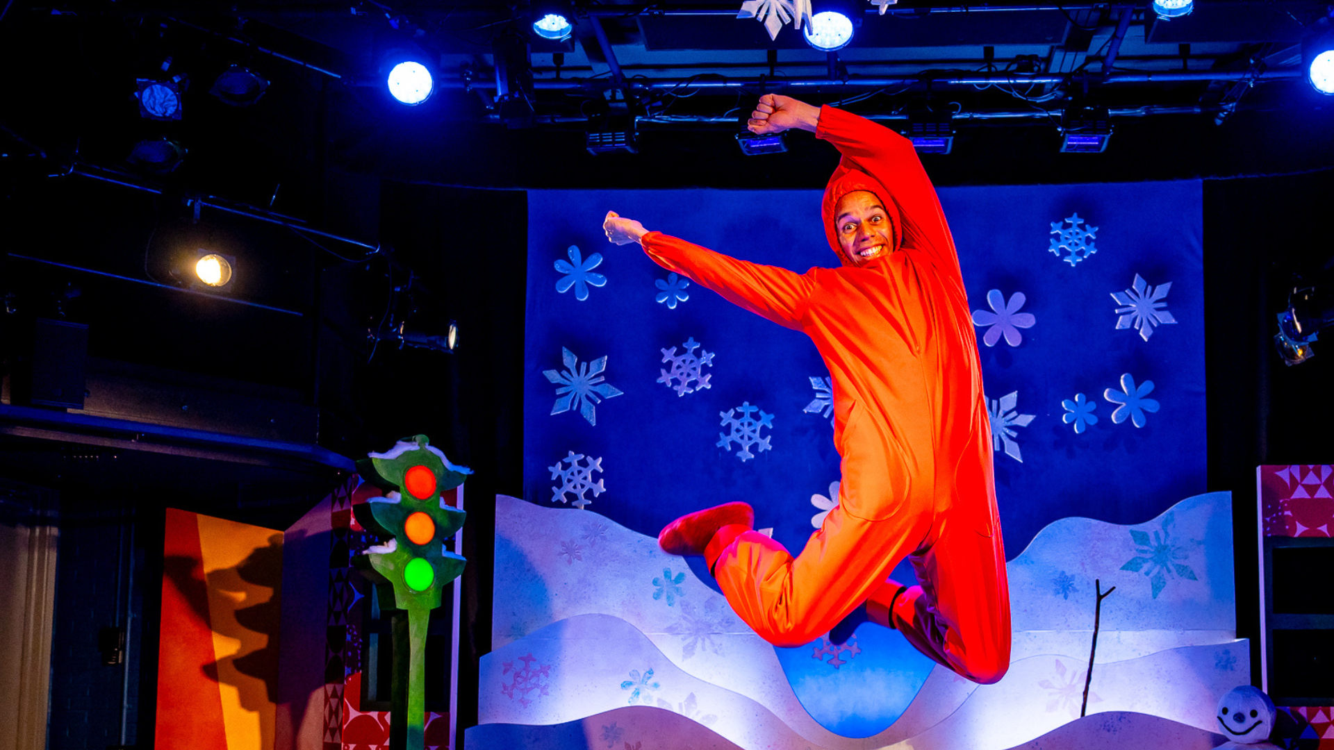 A Polka staff member wearing an orange snowsuit jumping in the air with joy. In the background is a snowy backdrop.