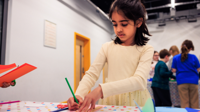 A child at a table using coloured pencils.