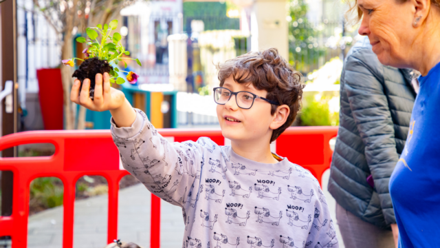 A child holding a plant that is ready to be potted.