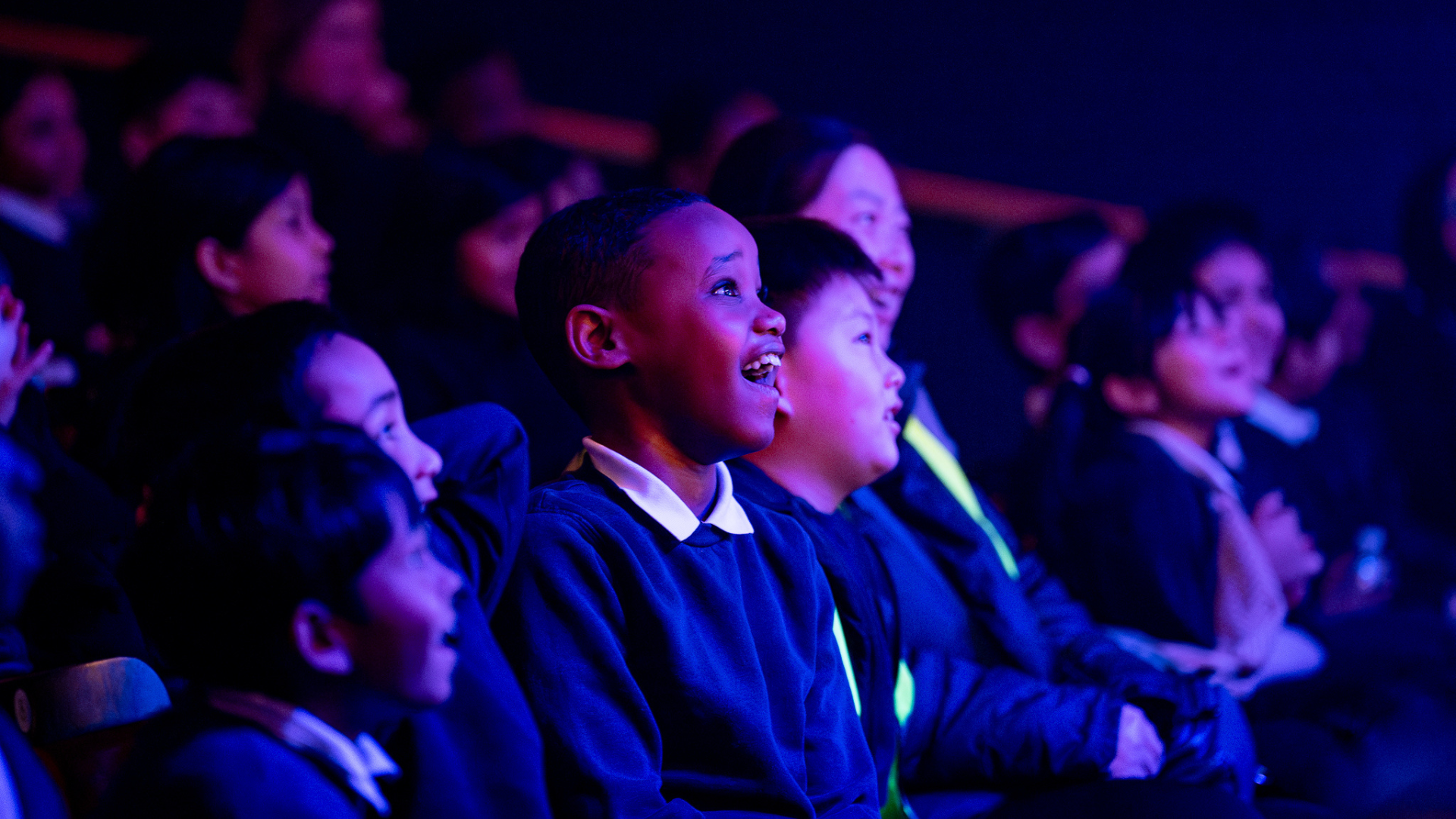 A group of children sat in the audience looking engaged with a performance.