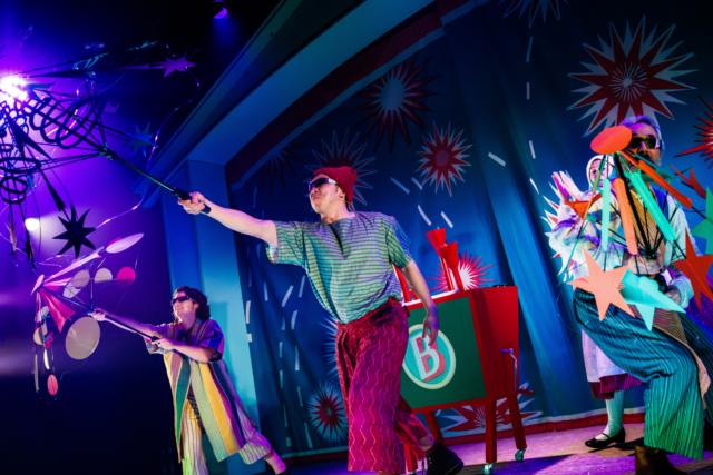 A group of performers onstage holding prop fireworks made from card.