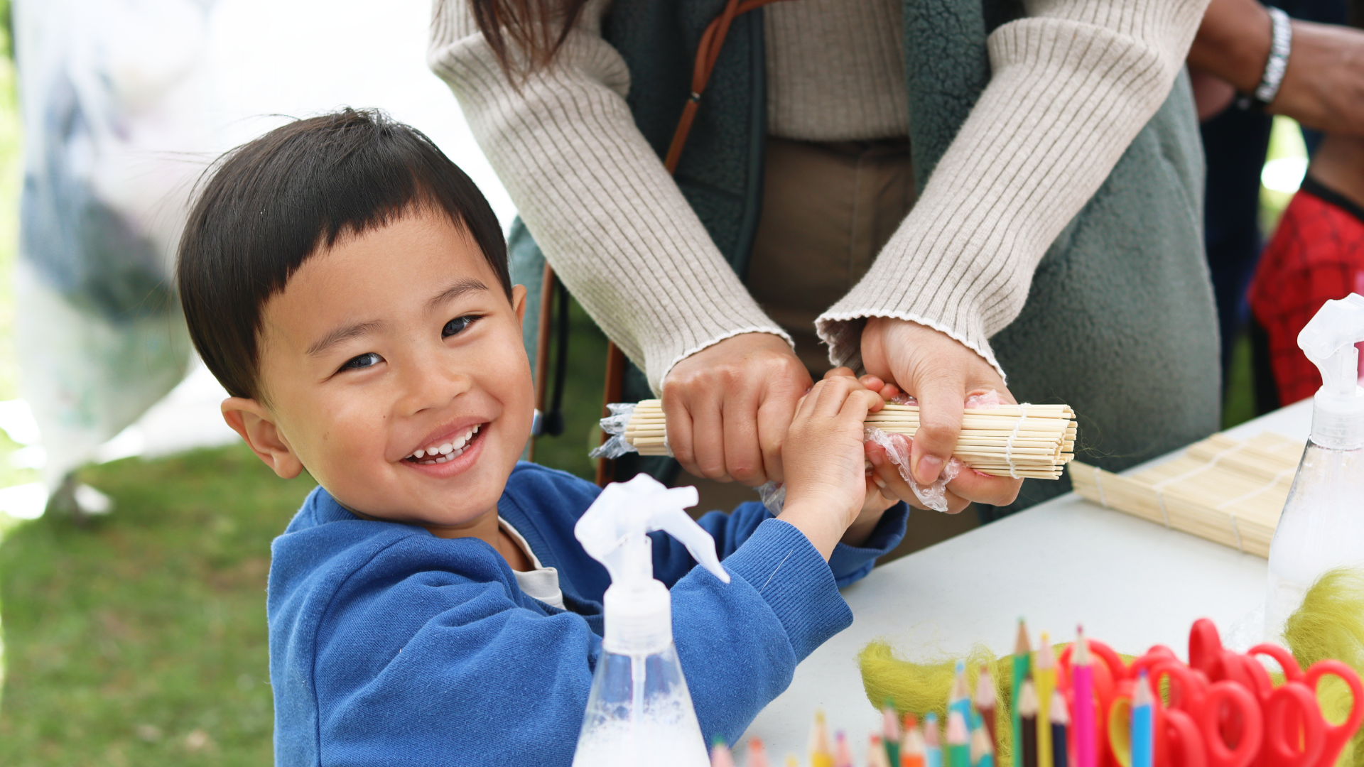 A small child holding wooden sticks at a crafts table.