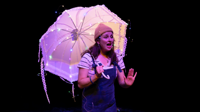 A performer mid dialogue holding a white umbrella.