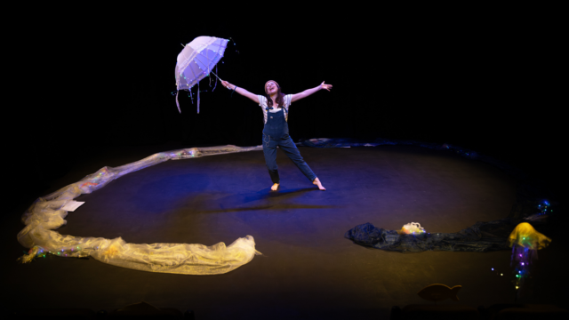 A performer holding an umbrella whilst dancing with their arms stretched out.