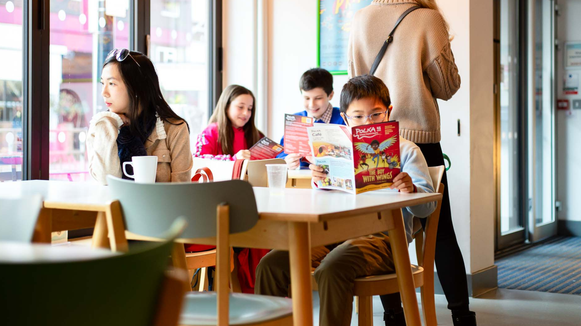 A mother and son sat in the cafe. The son is reading the Polka programme.