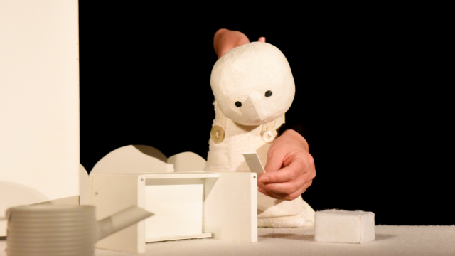 A puppeteer holding a white humanoid puppet.