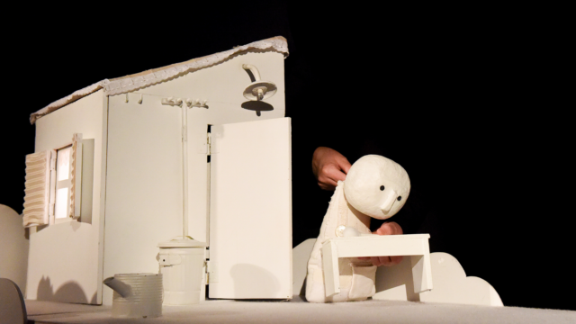 A puppeteer holding a white humanoid puppet.